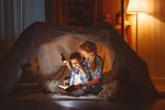 Mutter und Kind lesen im Licht von Taschenlampen unter einer Zeltplane, Foto stock.adobe.com © JenkoAtaman