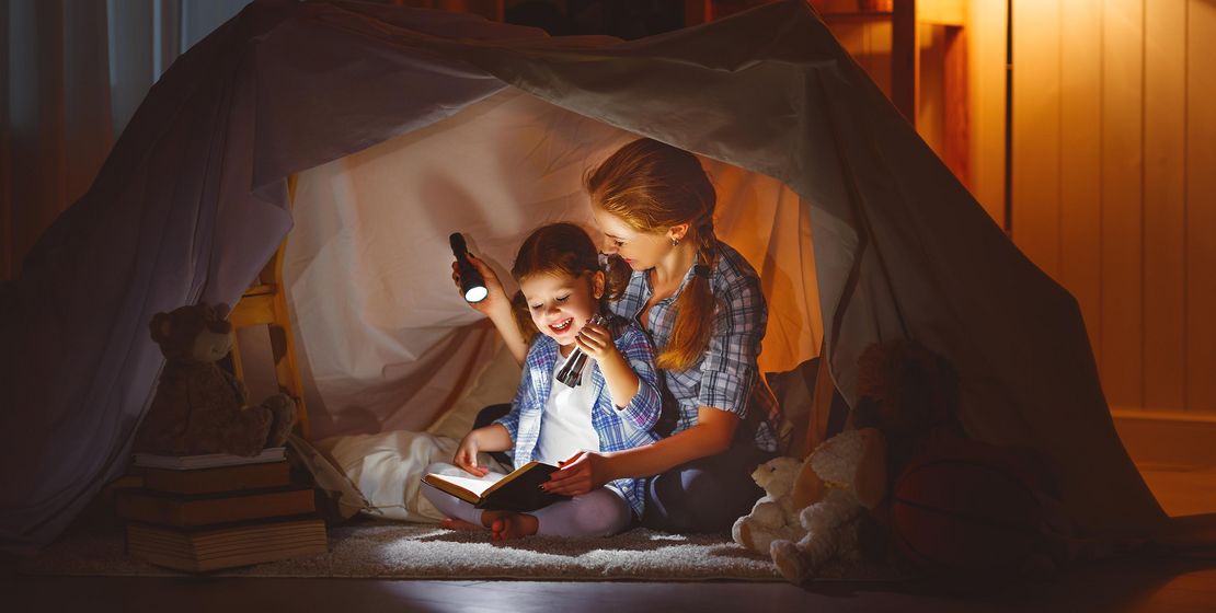 Mutter und Kind lesen im Licht von Taschenlampen unter einer Zeltplane, Foto stock.adobe.com © JenkoAtaman