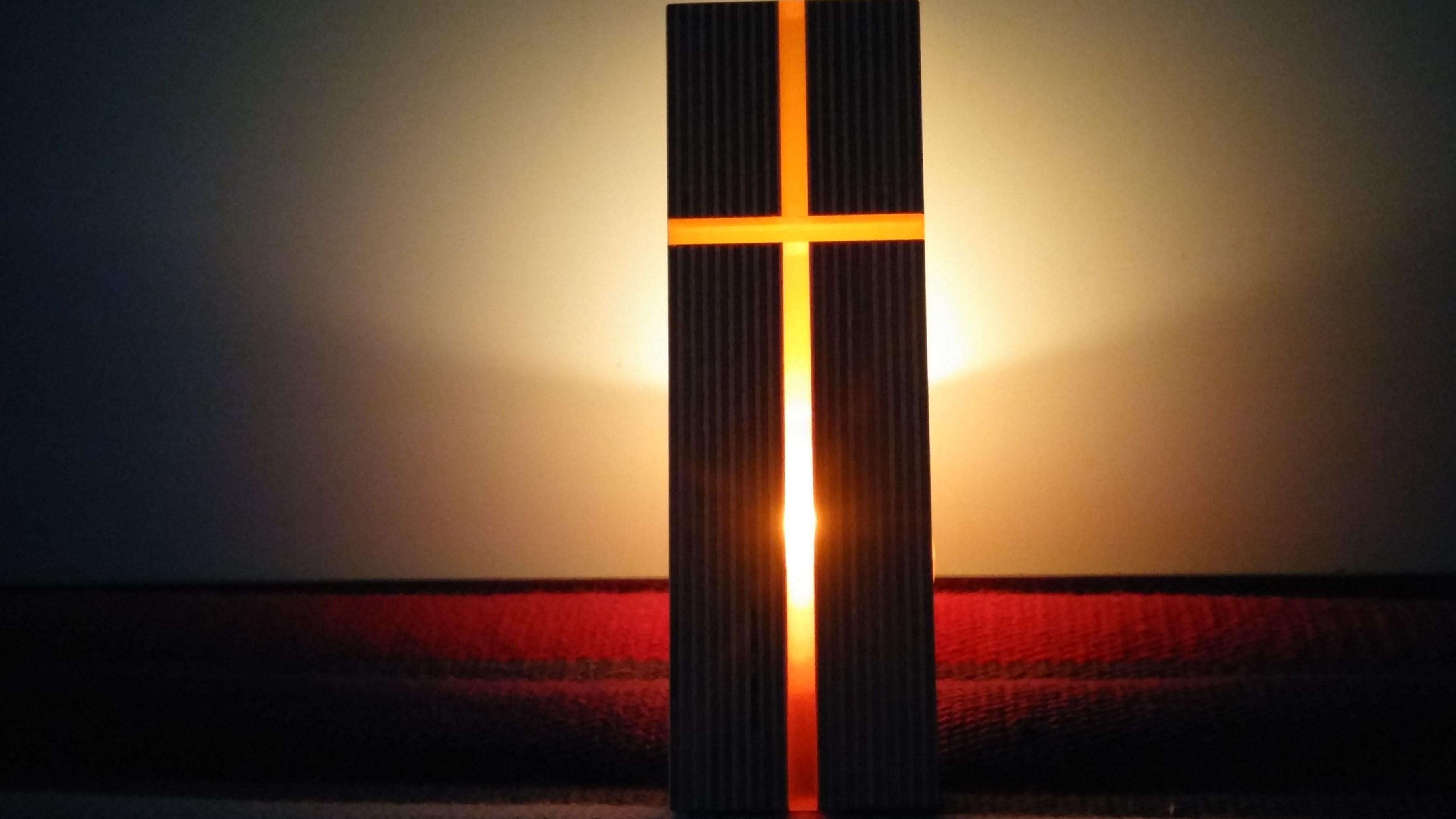 Ein Kreuz von hinten mit Kerzenlicht durchleuchtet
